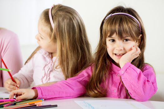 Portrait of Cute little girl at home. The other little girl drawing with colored pencils.