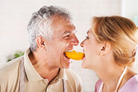 Senior Couple having fun in the kitchen and eating yellow peppers.
