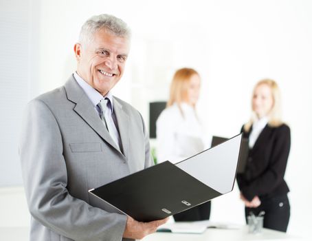 Happy senior businessman with folder standing in the office. Looking at camera. Selective Focus.