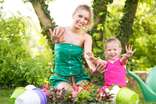 Beautiful mother and daughter planting flowers in the garden and showing dirty hands.