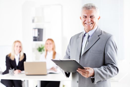 Happy senior businessman with documents standing in the office. Looking at camera. Selective Focus.