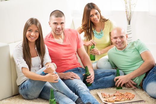 Friends enjoying eating pizza and drink a beer together at home party.
