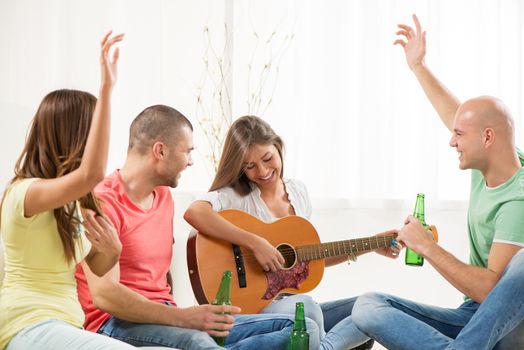 Four friends enjoying with guitar and beer together at the home party.