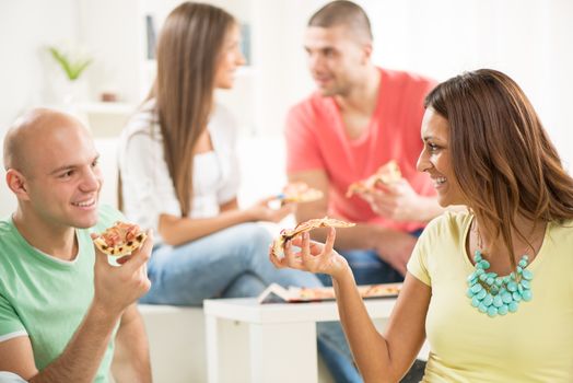 Four friends enjoying to eating pizza together at home party.