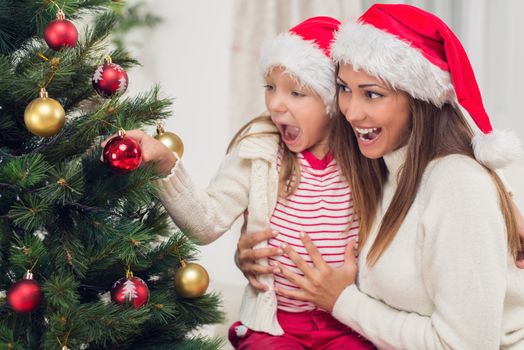 Young mother and her daughter decorating Christmas tree at home. 