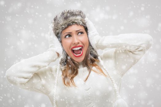 Cheerful beautiful young woman in warm clothing having fun while snowing.