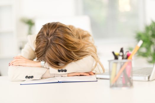 Young businesswoman napping on her desk next to documents late in the office.