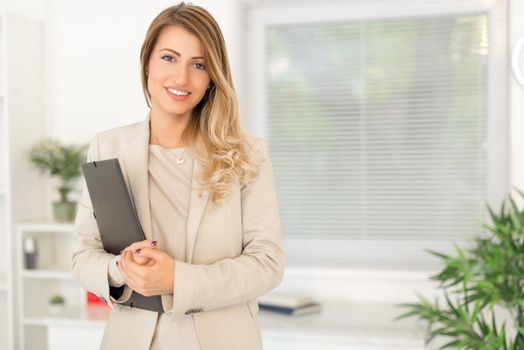 Beautiful young businesswoman standing in office with folder. Looking at the camera. 