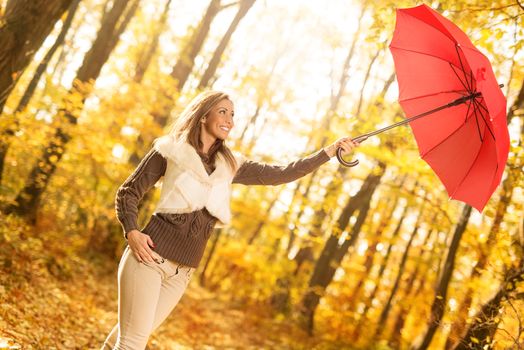 Beautiful cheerful young woman with red umbrella having fun in sunny forest in autumn colors.