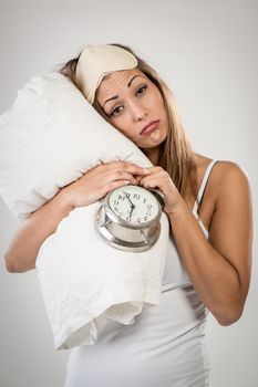 Beautiful young woman holding alarm clock and pillow. She is tired and lazy in morning.