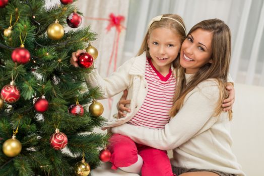 Young mother and her daughter decorating Christmas tree at home. 