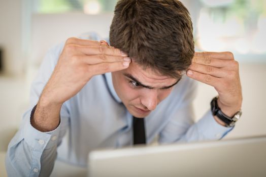 Frustration young businessman sitting in the office and looking at laptop.