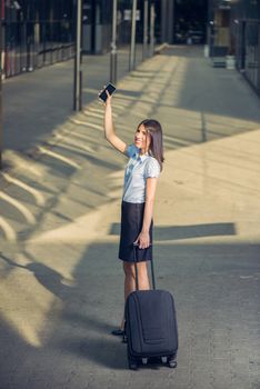 Young beautiful business woman walking with suitcase ready for a business trip and waving goodbye on outdoor.