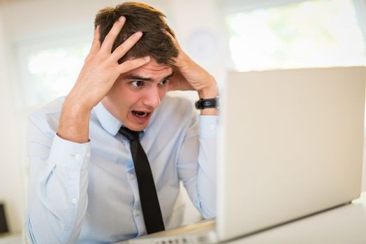 Frustration young businessman sitting in the office and looking at laptop.