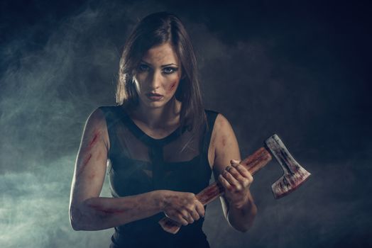 Beautiful dangerous girl with rusty axe. Looking at camera.