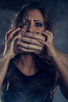 Young woman abuse victim with man's abuser hands on her mouth looking at camera