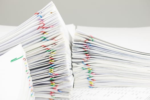 Colorful paper clip with pile of report place on finance account have blur pile of paperwork as foreground and background.