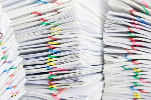 Close up colorful paper clip with pile of report have blur pile of paperwork as foreground and background.