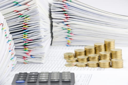Step pile of gold coins on finance account have blur calculator as foreground and pile of paperwork as background.