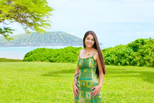 Beautiful biracial Asian Caucasian teen girl standing on lush green lawn  in Hawaii with ocean in background 