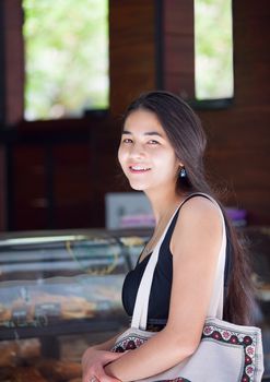 Beautiful biracial Asian, Caucasian, teen girl standing in line at cafe, smiling