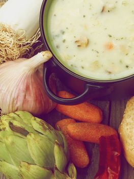 Healthy Artichoke Creamy Soup with Leek, Carrot, Garlic and Cheese in Dark Blue Pannikin closeup on Rustic Wooden background. Retro Styled