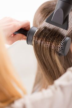 Drying long brown hair with hair dryer and round brush. Close-up.