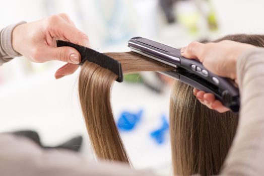 Hairdresser straightening long brown hair with hair irons.