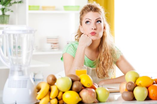 Beautiful young woman in a kitchen with fruits, thinking. Looking at camera.