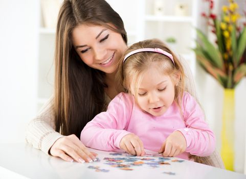 Mother and daughter playing at home. They assembling Jigsaw Puzzle.