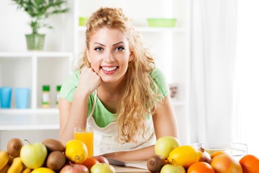 Beautiful young woman in the kitchen with fruits. Looking at camera.