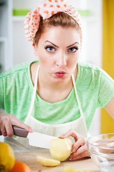 Beautiful young woman cutting apple in the kitchen. Looking at camera.