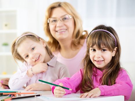 Two cute little girls drawing with colored pencils at home with Grandmother