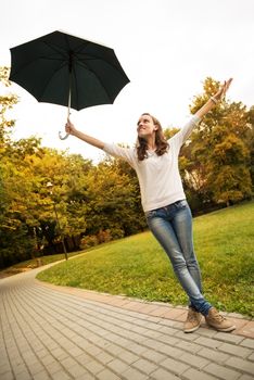 Young beautiful woman standing in rainy autumn park with umbrella and arms raised.