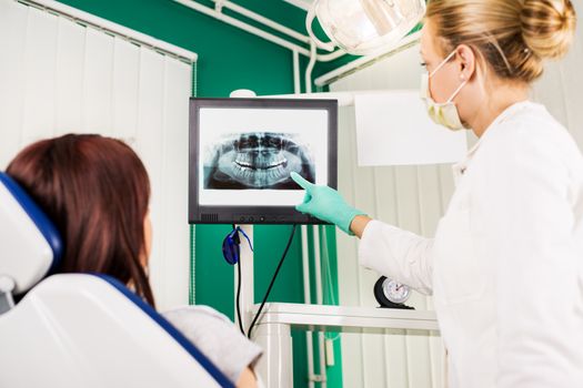 Young female dentist showing to the patient X-ray picture on LCD display.