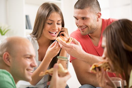 Four friends enjoying to eating pizza together at home party.