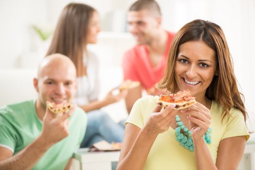 Close up of a young girl smiling and eating pizza with her friends in the background.