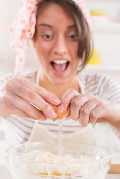 Cute young woman making dough in the kitchen. She is breaking eggs.