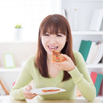 Asian woman eating pizza at home. Female living lifestyle indoors.
