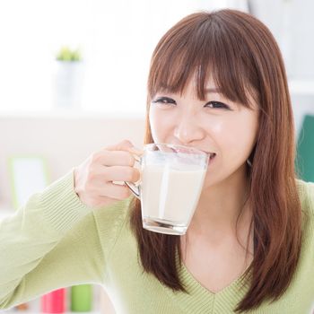 Portrait of happy Asian girl drinking milk as breakfast. Young woman indoors living lifestyle at home.