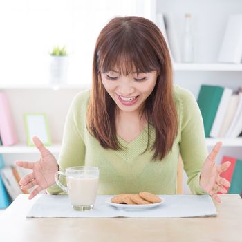 Asian woman feeling surprise with the breakfast, milk and cookies on dining table. Young girl indoors living lifestyle at home.