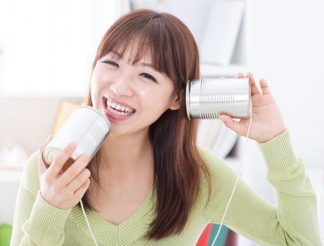 Happy Asian girl using old technology, talk and listen to communication cans. Young woman indoors living lifestyle at home.