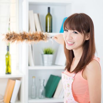 Happy Asian housewife with apron cleaning house, hand holding a duster and smiling. Young woman indoors living lifestyle at home.