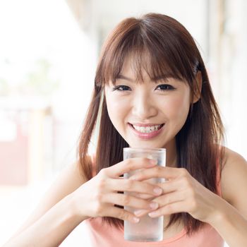 Happy Asian girl drinking mineral water at outdoor cafe. Young woman living lifestyle.
