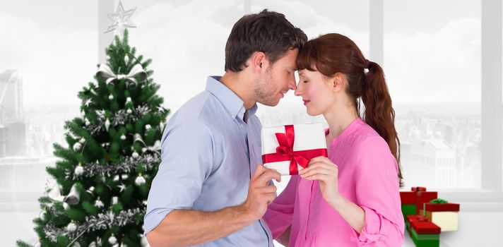 Loving couple holding a gift against home with christmas tree