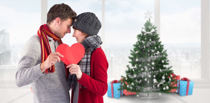 Couple holding a red heart against home with christmas tree