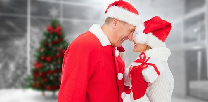 Festive mature couple holding gift against home with christmas tree