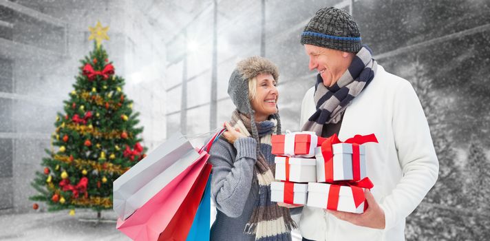 Festive mature couple holding christmas gifts against home with christmas tree