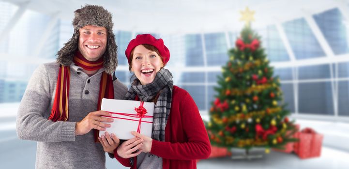 Couple smiling and holding gift against home with christmas tree