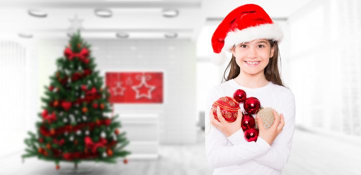 Festive little girl smiling at camera holding baubles against home with christmas tree
